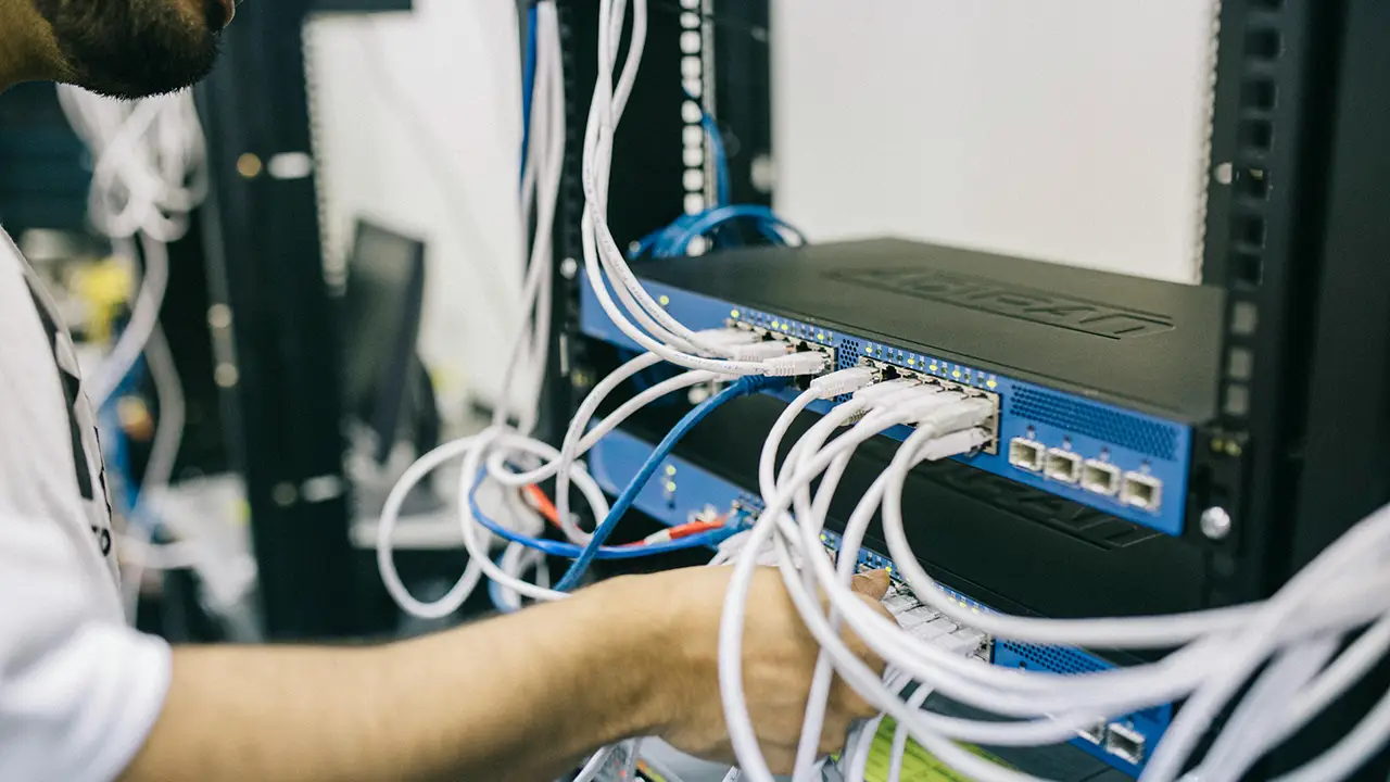 Ein Mann steckt ein Kabel in einen Netzwerkrouter der in einem Netzwerkschrank montiert ist