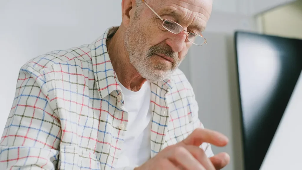 Ein älterer Mann mit Brille und kariertem Hemd schaut konzentriert auf ein Tablet und bedient es mit dem Finger.