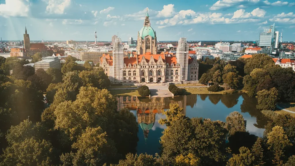 Panoramaaufnahme des Neuen Rathauses in Hannover mit Spiegelung im Wasser und Blick auf die Stadt im Hintergrund.