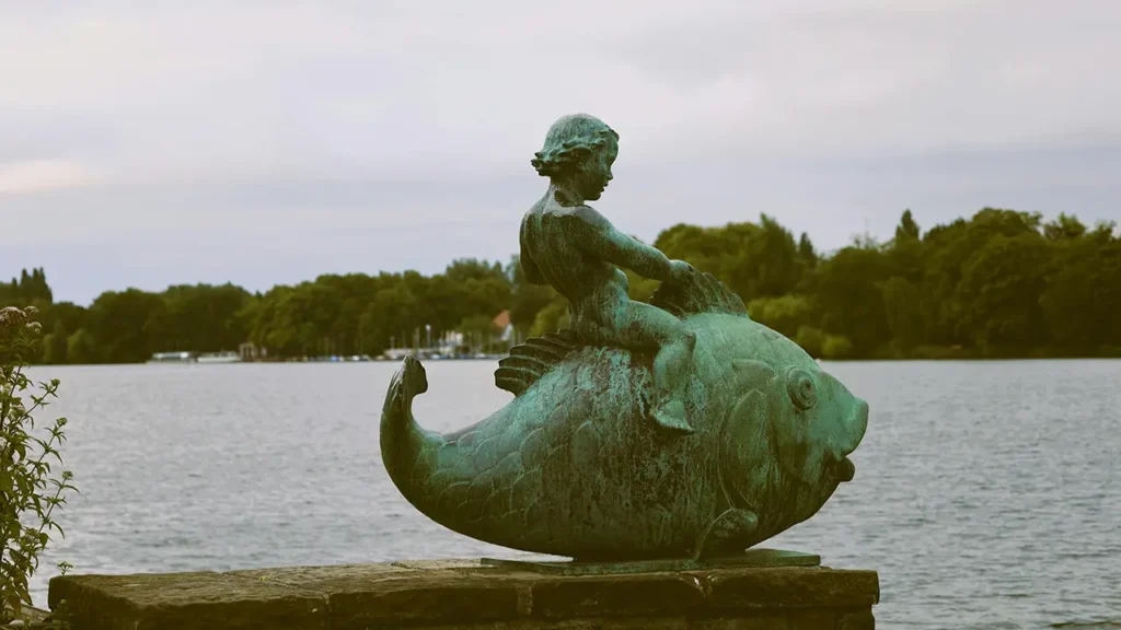 Bronzestatue eines Kindes auf einem Fisch am Ufer des Maschsees in Hannover