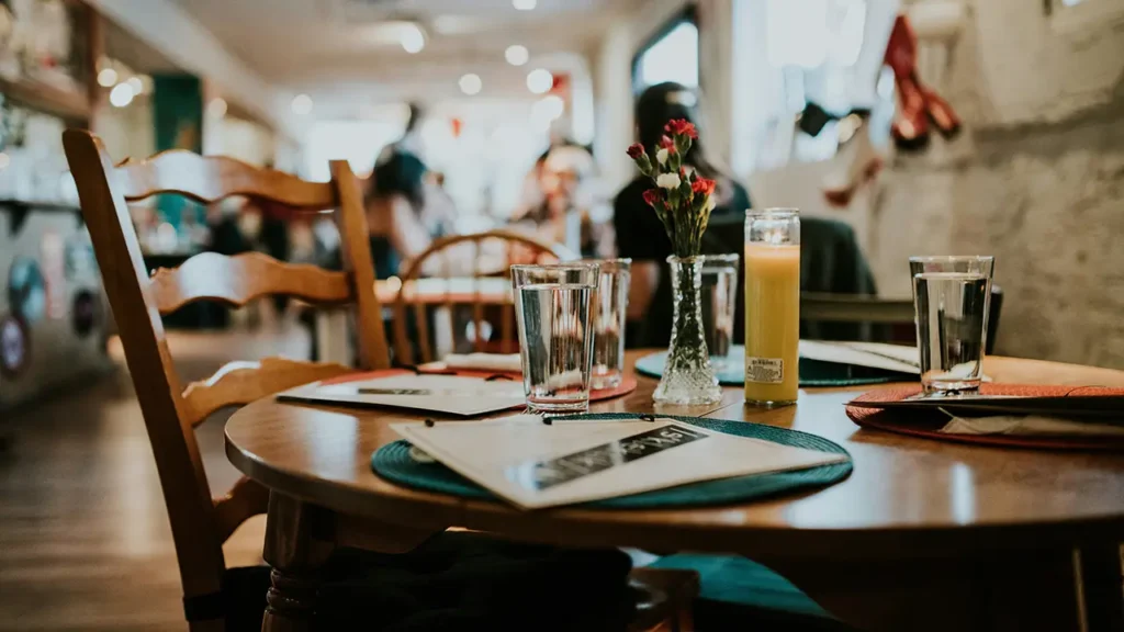 Restaurant Website erstellen: gedeckter Holztisch mit Speisekarten, Gläsern und Blumen im Restaurant-Ambiente